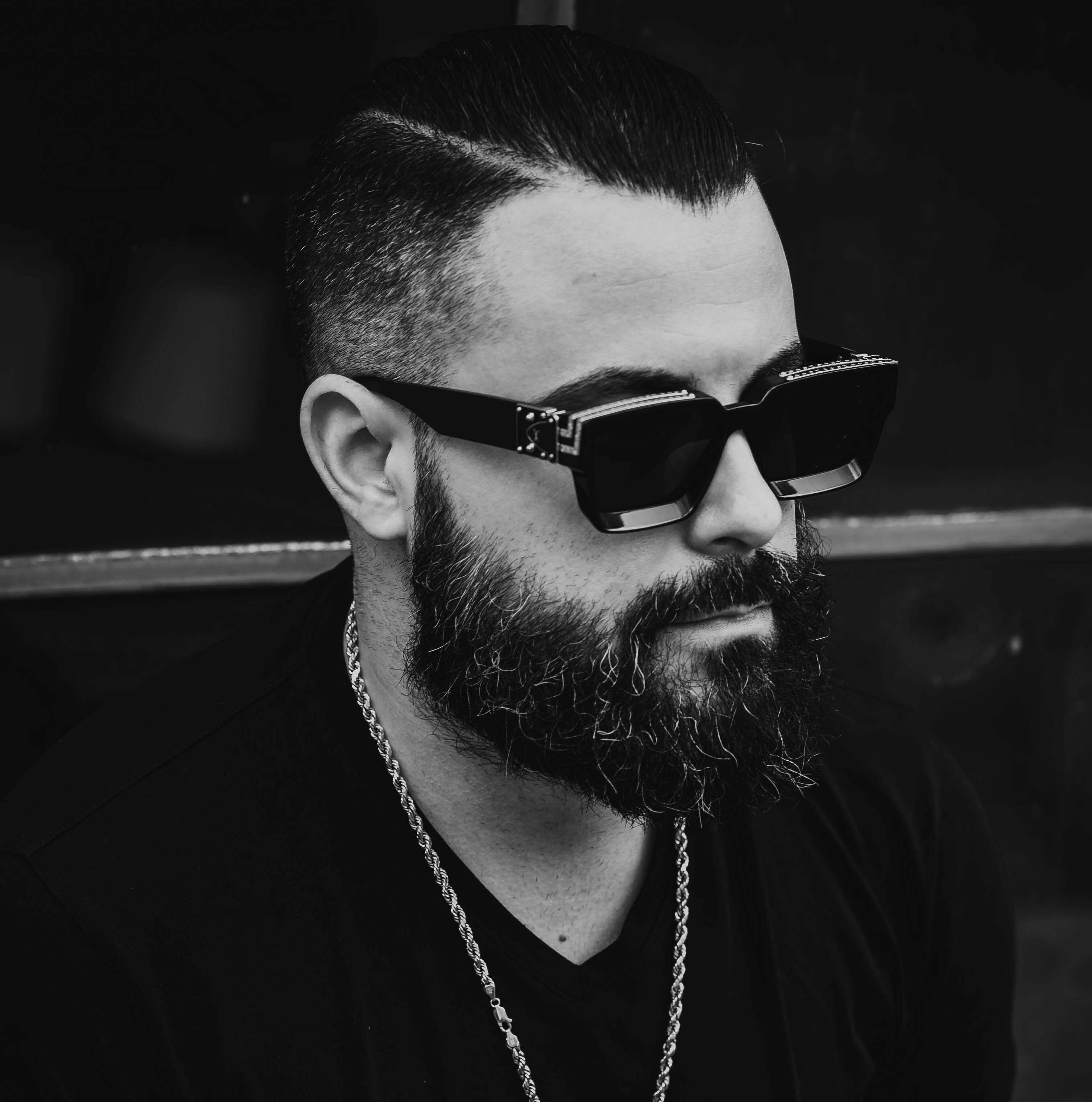 Man with thick salt and pepper beard wearing sunglasses and gold chain