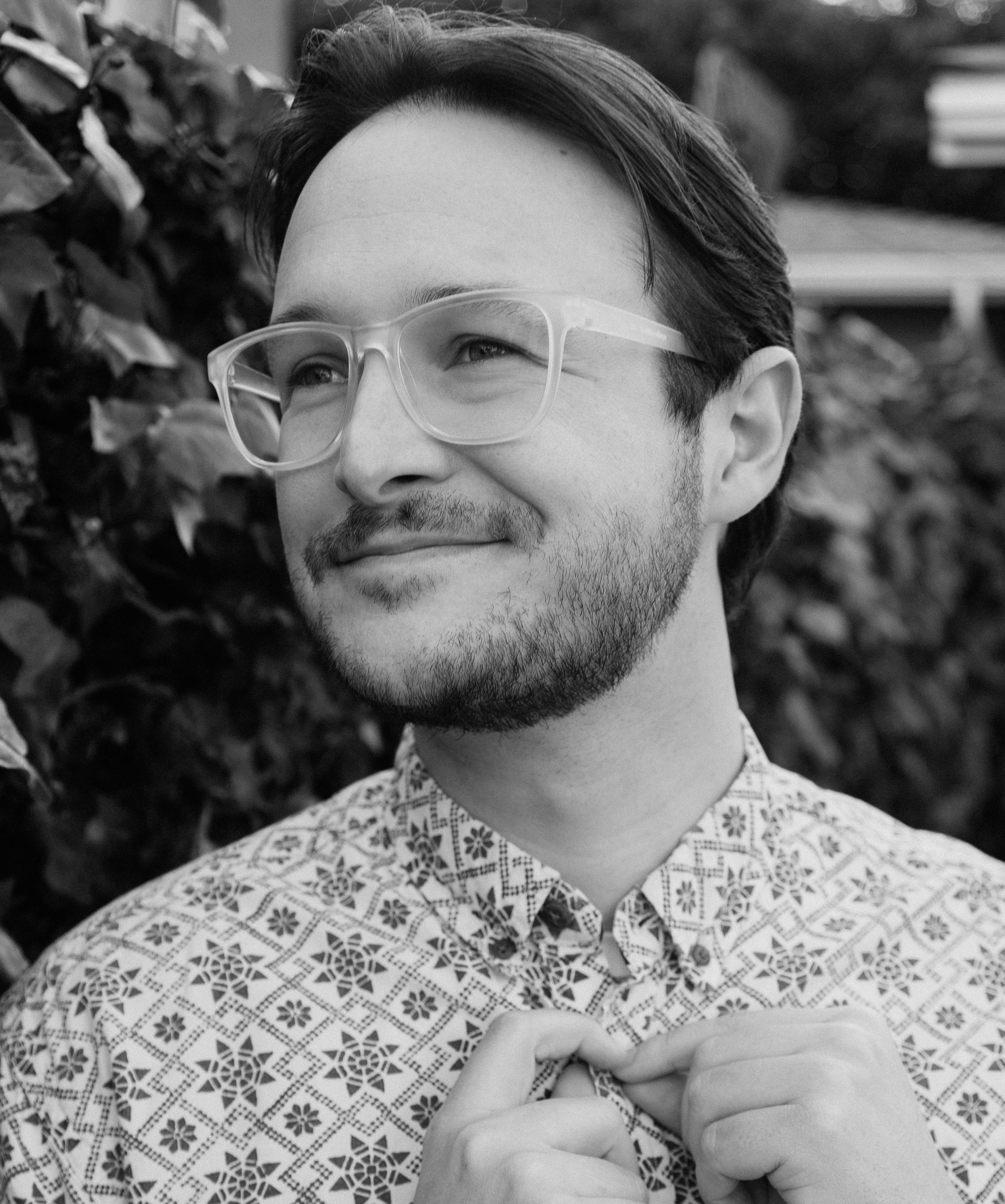 Young man with a five o'clock shadow beard wearing white frame glasses and button up shirt