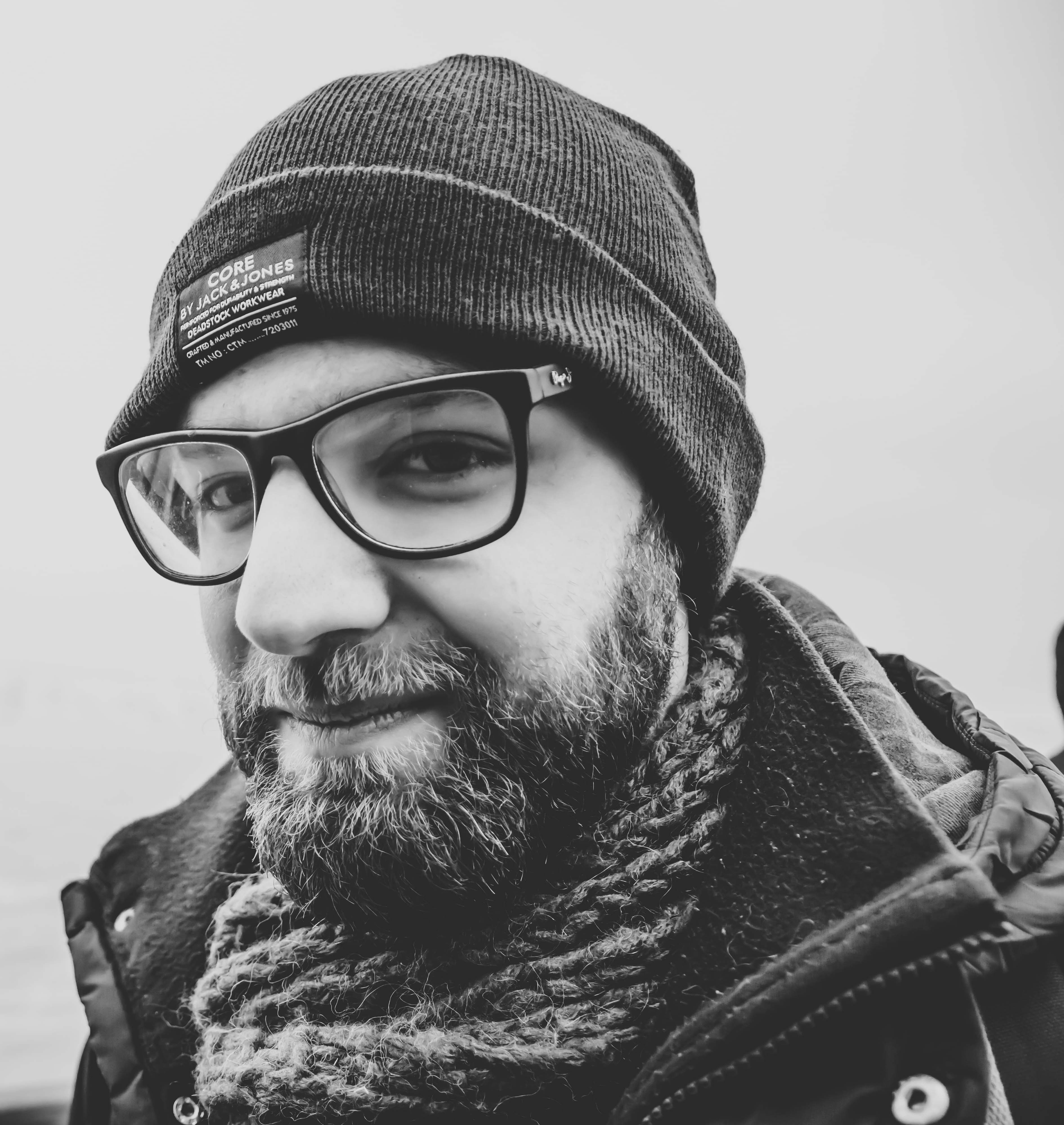Man with a thick, shor beard wearing a beanie and glasses, bundled in winter clothing